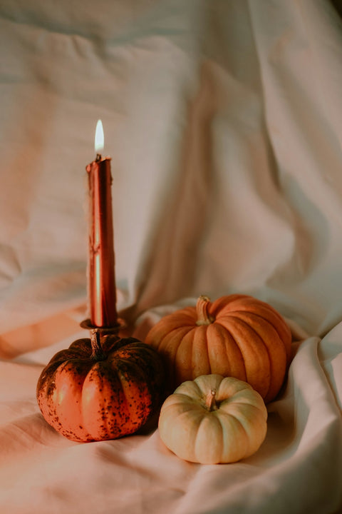 a candle and some pumpkins on a white sheet